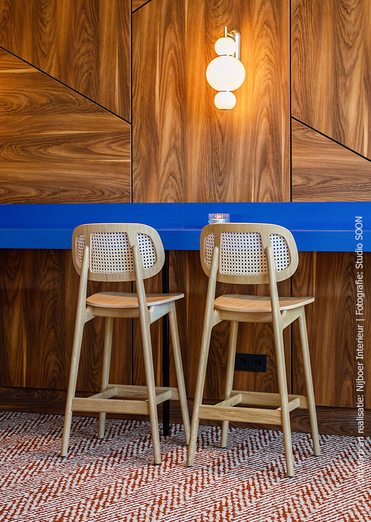 Wandafwerking met panelen waardoor een grafisch lijnenspel ontstaat. De wand is afgewerkt met decoratief plaatmateriaal met een warm houtdecor, De S016 Yosemite van Cleaf.