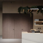 Een render van een horecagelegenheid met een bar uitgewerkt in het solid surface decor DM5048 Starstruck van Durasein, welke de luxe uitstraling van marmer op een warm witte basis biedt. De wandafwerking uitgewerkt in de FD29 Taranta van Cleaf, welke de beleving van zandsteen geeft, en een deur in de FD14 Taranta van Cleaf, een bruine steentextuur.