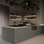 Zijaanzicht van een horecagelegenheid met een bar uitgewerkt in het donkergrijze plaatmateriaal FD16 Taranta van Cleaf in combinatie met een blad uitgewerkt in het gekorrelde solid surface decor TS053 Old Castle van Durasein. De wandafwerking uitgewerkt in het lichtgrijze decor FD16 Taranta van Cleaf met een deur in de S212 Corteccia, welke de beleving van gerookt grijs kastanjehout biedt.