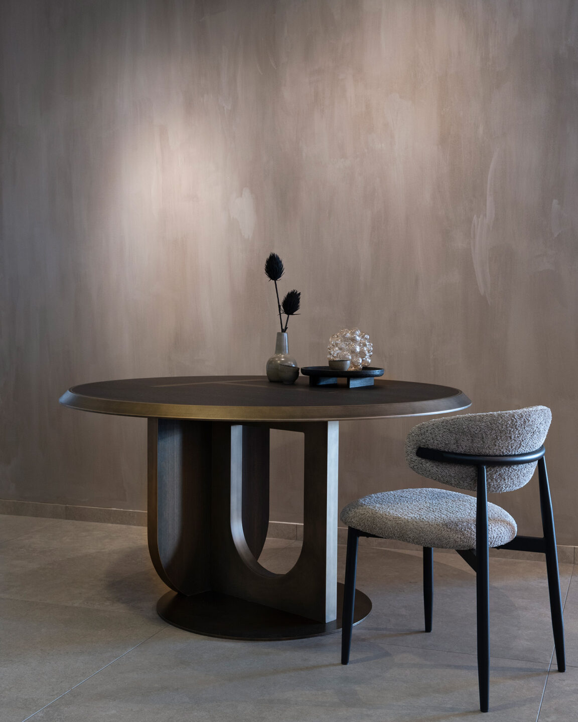 De ronde Icon tafel van Tio is gemaakt met decoratief plaatmateriaal van DecoLegno in donkerbruine kleur LR29 Sablé, met metalfinish rand met stoel en bloem op tafel