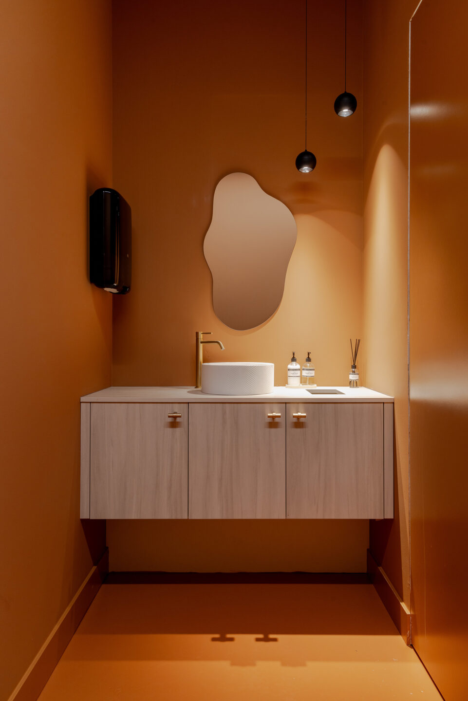 Wastafel in toilet in licht hout LS63 Ceppo met oranje wanden en organische spiegel.