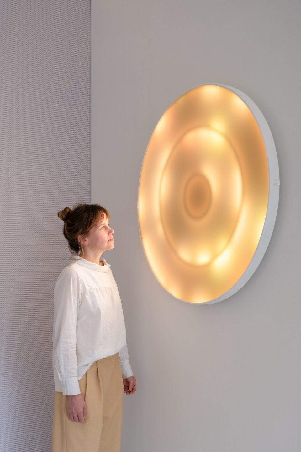 Dame kijkt naar Breathing Light van A+N Studio, een ronde witte lamp met warm licht