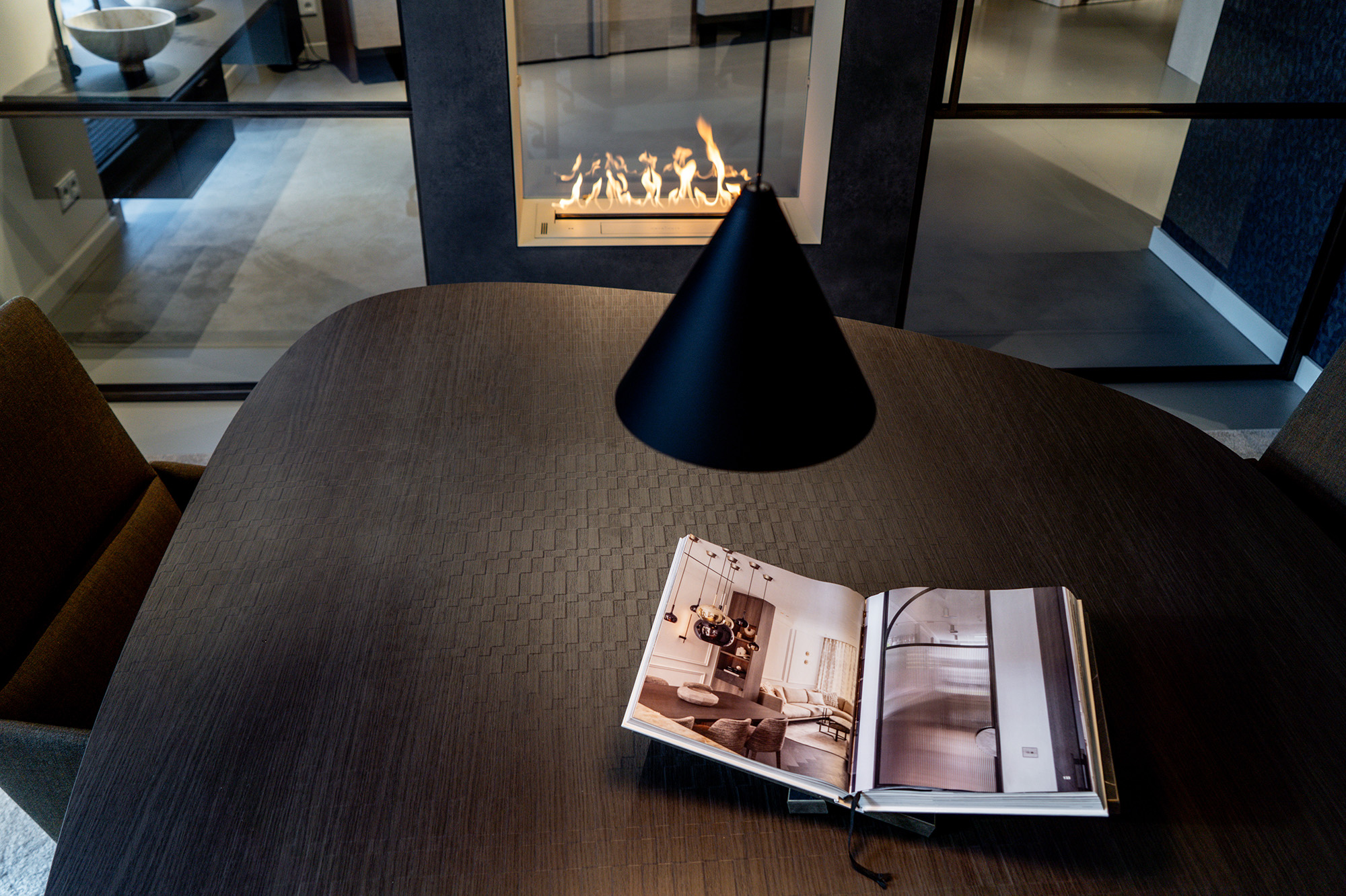 Foto van een tafel en lamp met op de achtergrond een brandende sfeerhaard