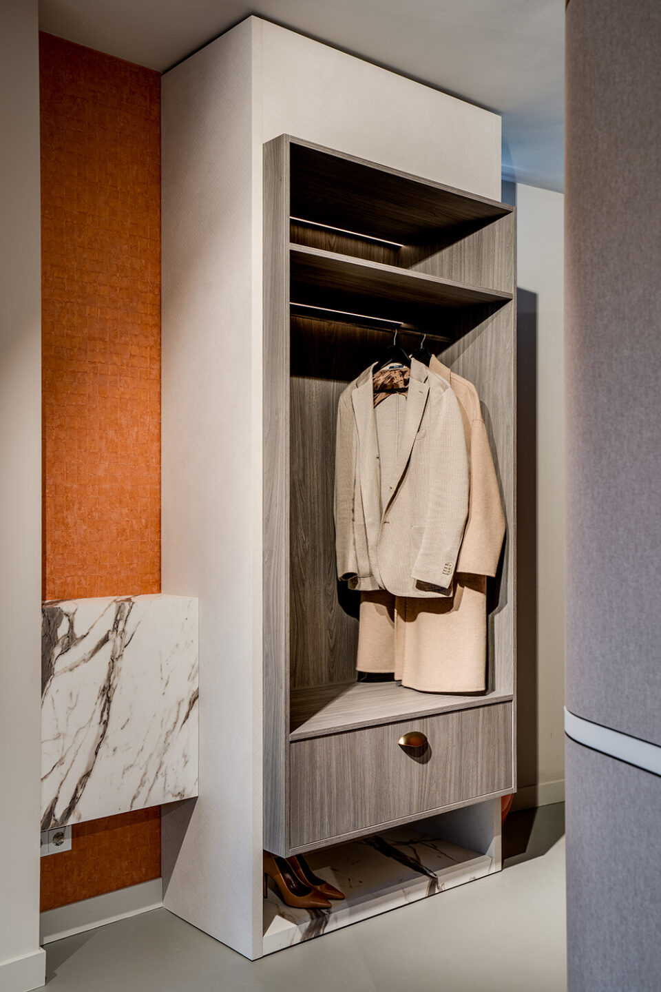 Maatwerkgarderobekast met jassen en oranje behang ernaast