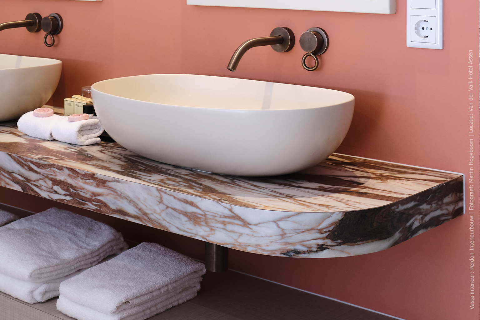 Wastafelmeubel met afgeronde vormen in marmerdecor D045 Fiocco, met warme bruin-witte aders tegen een roze wand.